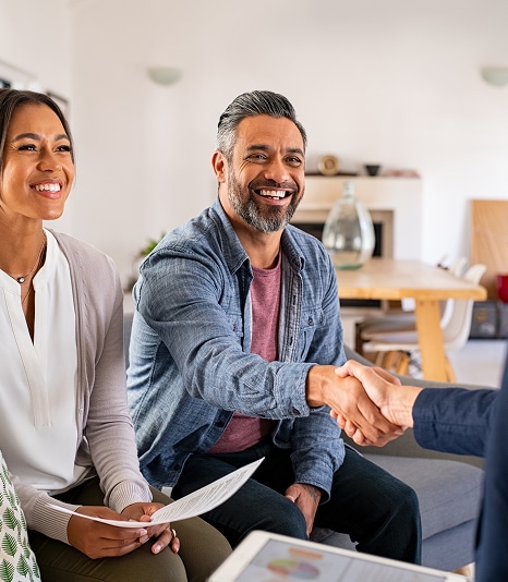 Couple souriant négociant ; l'homme serre la main d'un partenaire commercial devant une femme tenant des papiers.