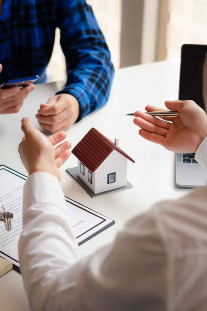 Signature contrat immobilier: clés et maquette de maison Mains tendues au-dessus d'une maquette de maison, un stylo est proposé près d'un contrat avec le mot "Signature" et des clés.