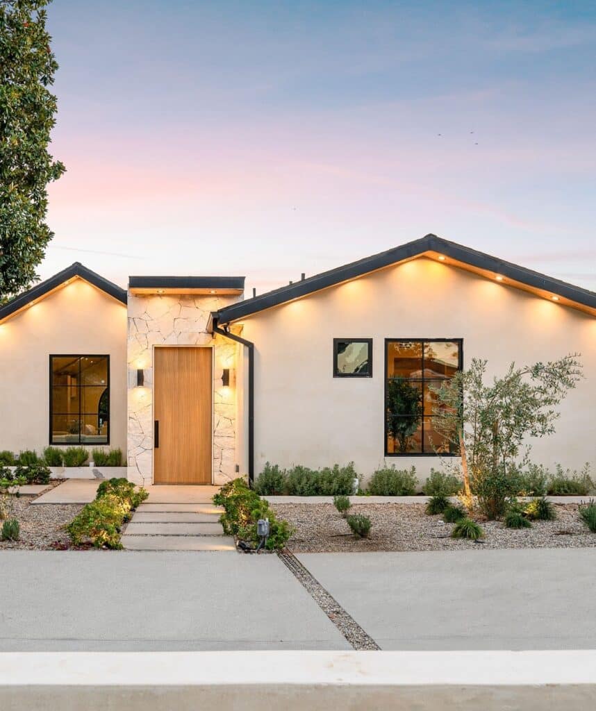 Facade moderne, pierre et bois, ambiance crepuscule Façade de maison moderne au crépuscule. Mur en stuc beige, entrée en pierre naturelle et porte en bois. Éclairage chaud sous les toits noirs.